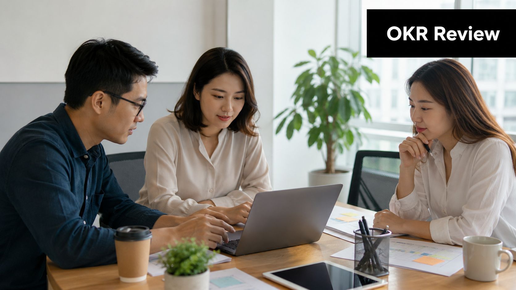A professional team of three colleagues reviewing OKR goals during a collaborative business meeting at a desk.